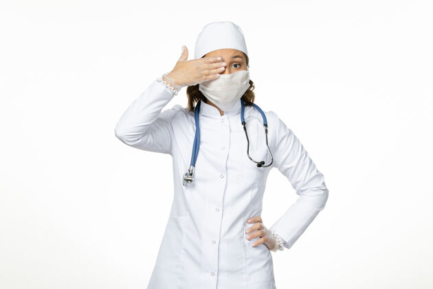 办公桌正面图女医生穿着白色医疗服 戴着口罩 由于白色办公桌上有冠状病毒大流行病毒病专业人员病毒人员