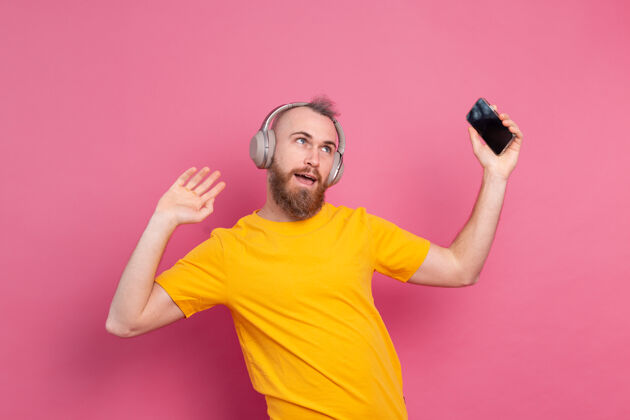 娱乐帅哥带着手机和耳机在粉色背景上翩翩起舞音乐歌曲耳机