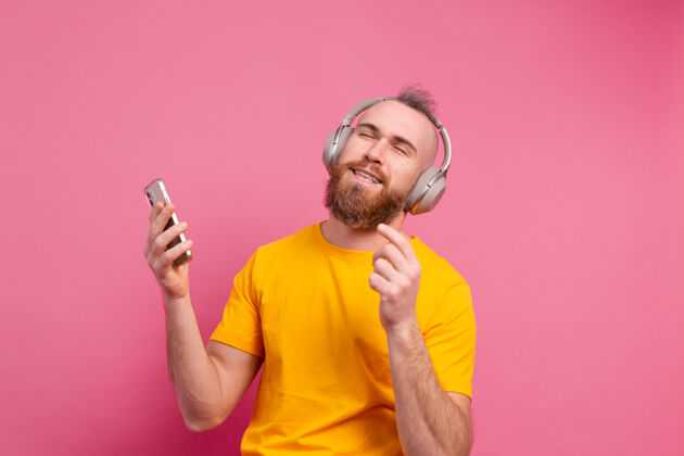 男人帅哥带着手机和耳机在粉色背景上翩翩起舞休闲乐趣人