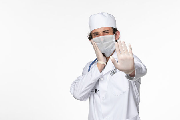 男性正面图：男医生穿着医疗服 戴着无菌口罩 以防白色桌面病毒冠状病毒大流行疾病穿着医生疾病