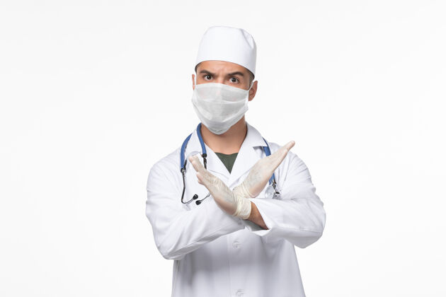 穿戴正面图：男医生穿着医疗服 戴着口罩 戴着听诊器 在白色办公桌上观察病毒-病毒-疾病大流行面罩正面防护