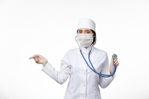 听诊器正面图女医生穿着白色无菌医疗服 戴着口罩因冠状病毒-使用听诊器对白墙病病毒冠状病毒-大流行性疾病套装使用大流行