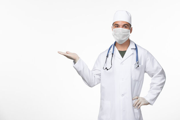 外套正面图：男医生穿着医疗服 戴着口罩 用听诊器对着白墙病毒-病毒-疾病大流行男性对抗听诊器