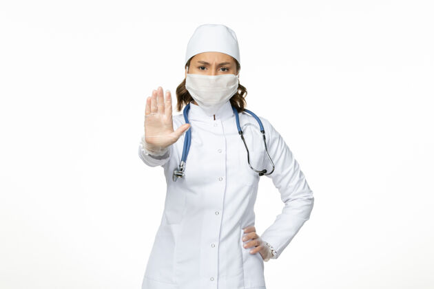 医疗正面图女医生穿着白色的医疗服 戴着口罩 由于白墙上有冠状病毒大流行性疾病隔离冠状病毒专业女性面罩