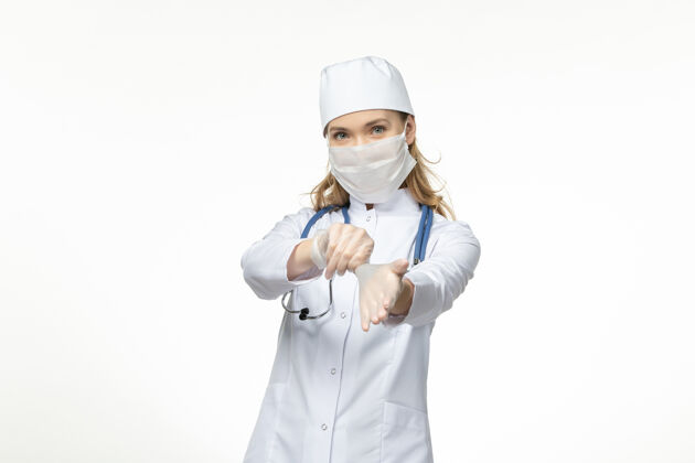 病毒正面图女医生穿着医疗服戴着口罩戴着手套因白墙上冠状病毒大流行的冠状病毒大流行专业制服