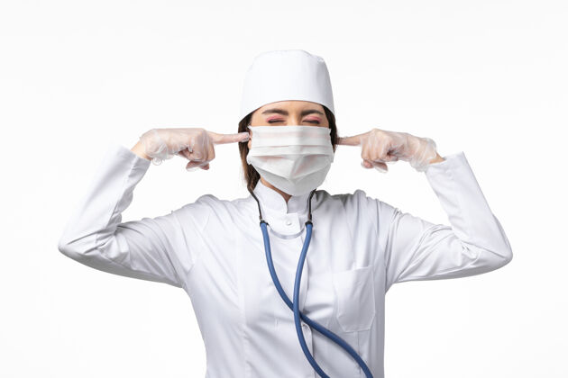 视图正面图：女医生穿着白色医疗服 戴着口罩 因大流行闭上了耳朵 白桌子上的病药病毒大流行 covid-桌子套装医疗