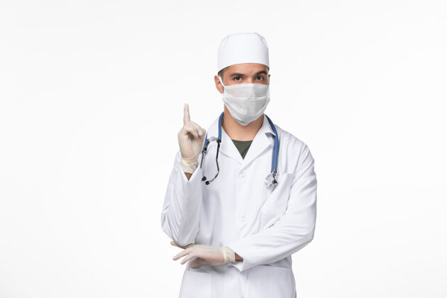 医疗正面图：男医生穿着医疗服 戴着口罩 用听诊器对着白色墙壁上的冠状病毒-疾病大流行病毒视图套装男性