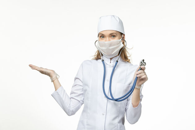 制服前视图穿着白色医疗服的女医生在白墙上使用听诊器疾病冠状病毒-大流行性疾病正面使用专业人员