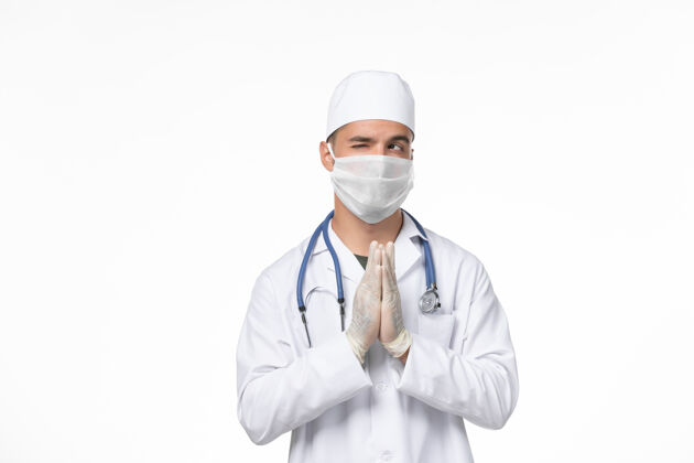 正面正面图：男医生穿着医疗服 戴着口罩 对抗白色墙壁上的冠状病毒药物大流行冠状病毒专业医生