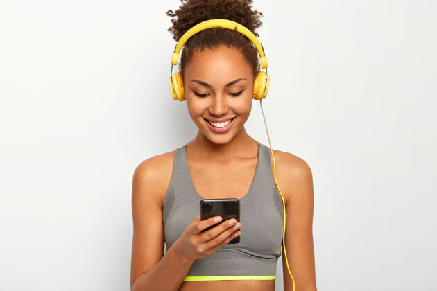 放松快乐的运动型卷发非裔美国妇女戴着耳机听音乐 笑容灿烂 戴着运动胸罩听高兴女人