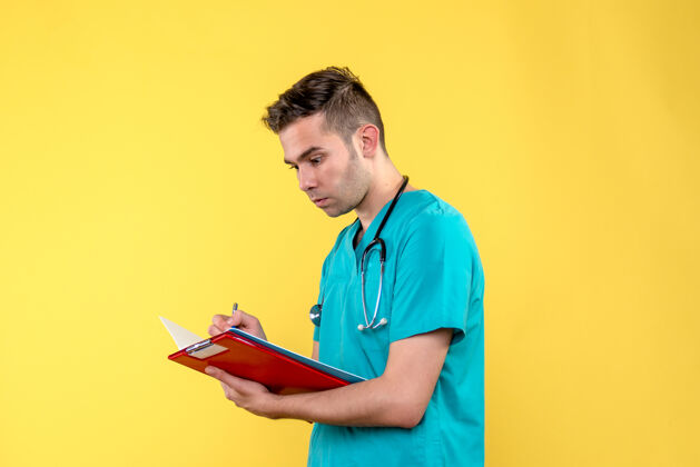 写作年轻男医生在黄色墙上写笔记的正面图听诊器帅气成人