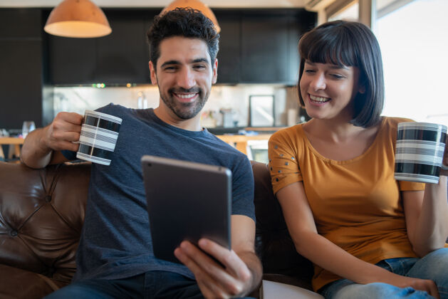 通信一对年轻夫妇坐在家里的沙发上 用数字平板电脑进行视频通话的肖像呆在家里新的正常生活方式概念聊天共享互联网