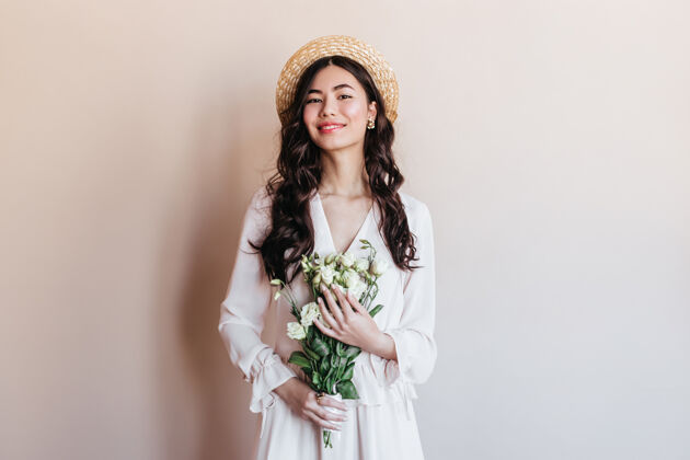 积极拿着白花的亚洲女人在笑戴草帽的日本女人拿着花束摆姿势的正面图卷曲草帽深色