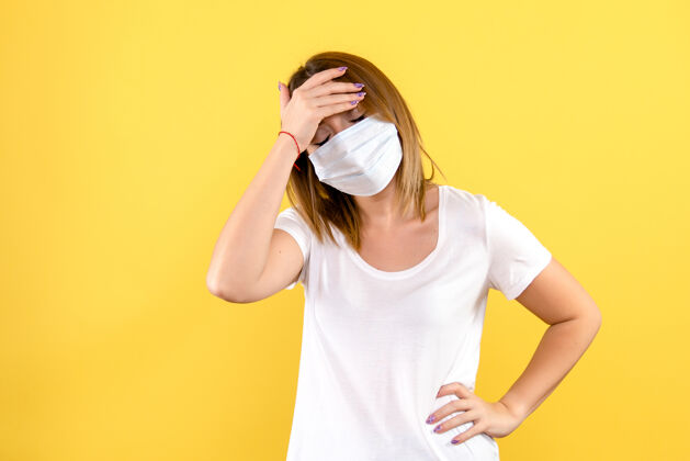 运动装黄色墙壁上戴着面具的年轻女子的正视图正面冠状病毒成人