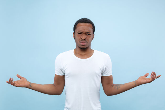 衬衫半身特写肖像的年轻非洲裔美国男子在白色衬衫的蓝色空间人类的情感 面部表情 广告概念事业表情面部
