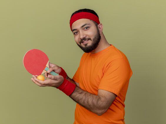 持有高兴的年轻人戴着头带和手环拿着乒乓球拍男子运动乒乓球