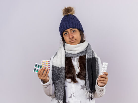 不愉快未出狱的生病的年轻女孩戴着冬天的帽子 戴着围巾 手里拿着白色的隔离药片围巾药丸女孩
