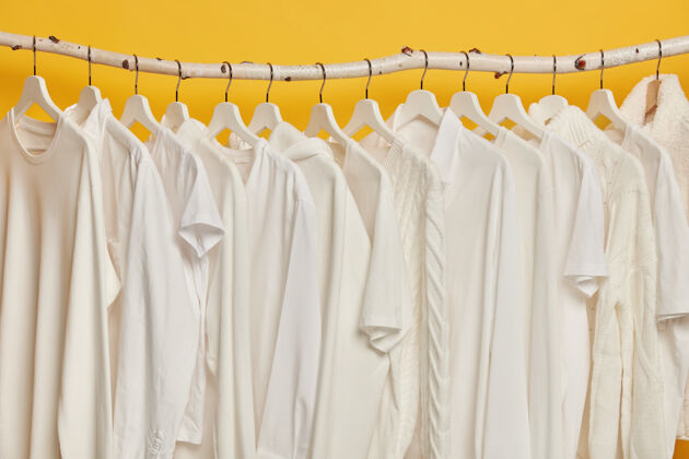 焦点同样的白色衣服放在壁橱的木架上衣架上的衣服收藏 隔离在黄色背景上零售商店白色