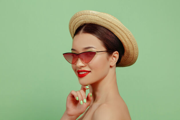 女人美丽女人的画像 明亮的妆容 红色的眼镜和帽子在绿色空间时尚和时尚的制作和发型夏天的颜色健康漂亮严肃