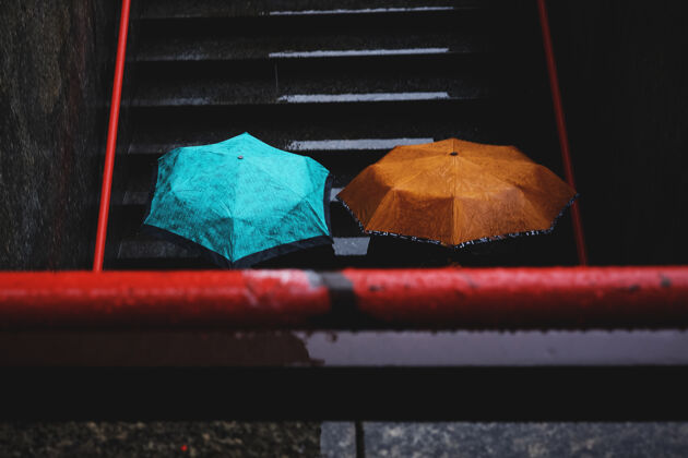 城市两个人拿着蓝绿色和棕色的雨伞潮湿楼梯街道