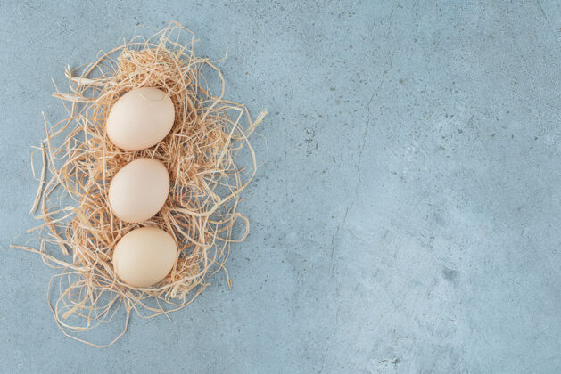 鸡蛋一小捆鸡蛋放在大理石背景上的一小堆稻草上高质量的照片口感有机营养