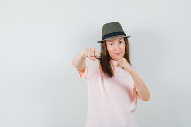 帽子年轻的女性站在战斗姿势在粉红色的t恤 帽子和看起来自信 前视图年轻姿势漂亮