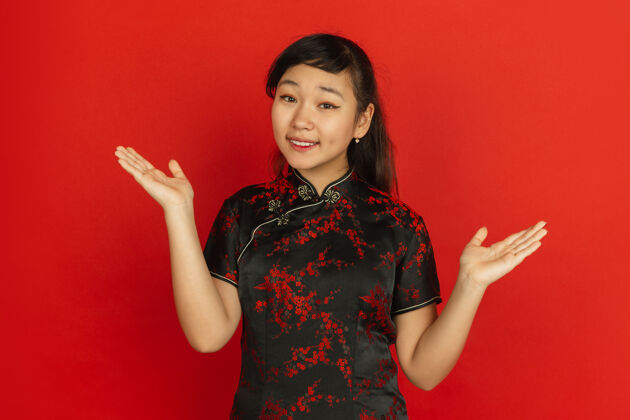 欢呼做手势 邀请客人中国新年快乐红色背景上的亚洲少女肖像穿着传统服装的女模特看起来很快乐庆祝 人类情感复制空间微笑节日文字空间