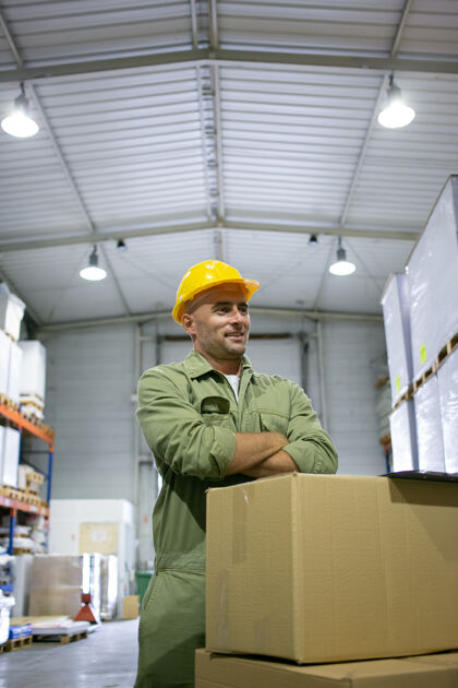 工业积极的蓝领工人戴着黄色安全帽 站在一堆箱子前 双臂交叉 面带微笑垂直射击劳动理念盒子工厂工人