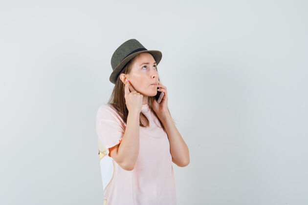 说话穿着粉色t恤 戴着帽子 面带沉思的年轻女孩在讲手机前视图童年小年轻