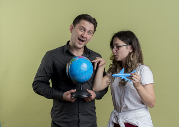 男人一对快乐的年轻游客 一男一女手持地球仪和玩具飞机 一起站在轻墙上飞机抱着年轻