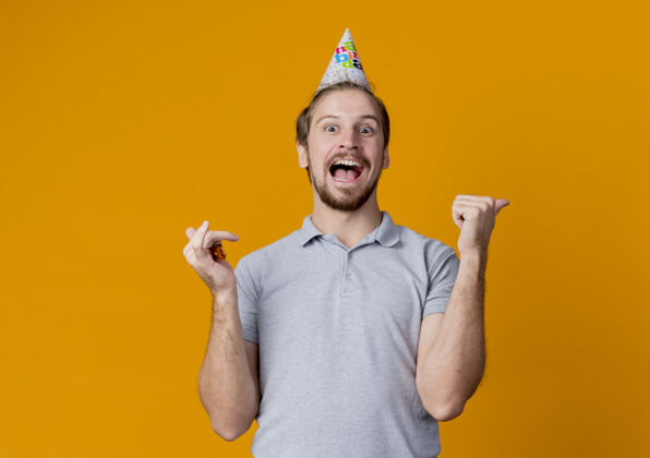 兴奋快乐的年轻人戴着节日帽庆祝生日聚会疯狂快乐兴奋地站在橙色的墙上庆祝帽子站立