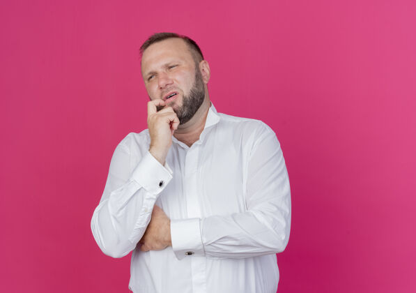 男人一个留着胡子的穿白衬衫的男人站在粉红色的墙上 困惑地看着一边站拼图成年人