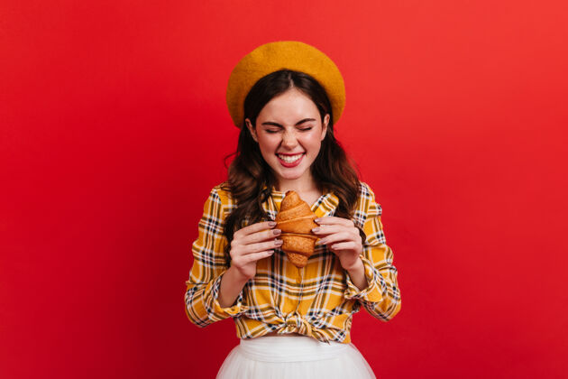 手势快乐的女孩期待地看着刚烤好的羊角面包红墙上穿着橙色贝雷帽和白色裙子的女士的画像人年轻贝雷帽