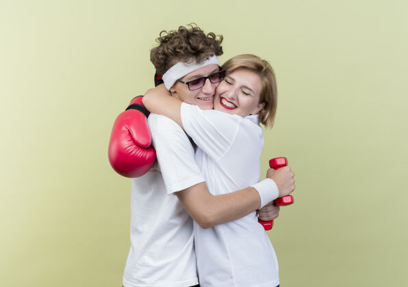 拥抱年轻的运动型情侣戴拳击手套的女人抱着戴拳击手套的男朋友快乐而积极地站在轻墙上积极运动立场