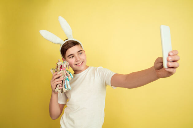乐趣自拍玩具白人男孩作为复活节兔子在黄色工作室背景复活节快乐的问候时尚信心面部