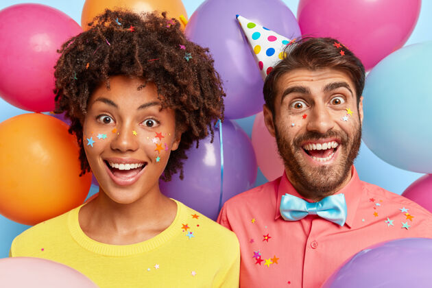 帽子快乐快乐的年轻夫妇在生日彩球的簇拥下摆姿势快乐肖像友谊