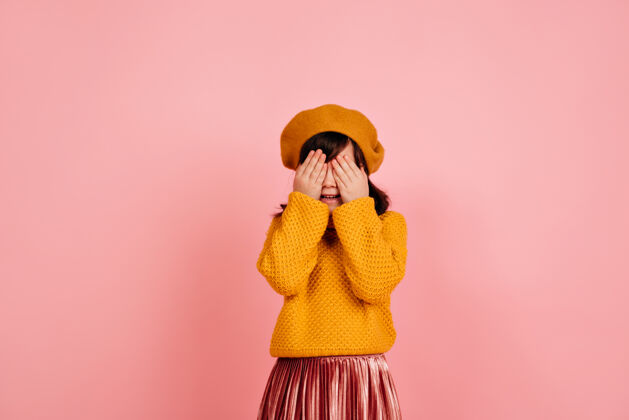 乐趣孩子把脸藏在粉红色的墙上孩子毛衣时尚