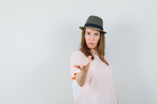 休闲身穿粉色t恤的年轻女性 戴着帽子 伸着手做着困惑的手势 俯视前方姿态民族拼图