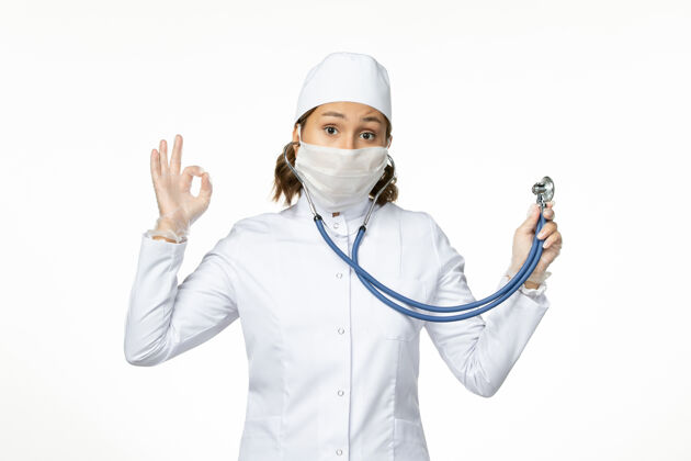 大流行正面图年轻女医生戴着无菌口罩由于冠状病毒手持听诊器在白色表面冠状病毒制服医疗