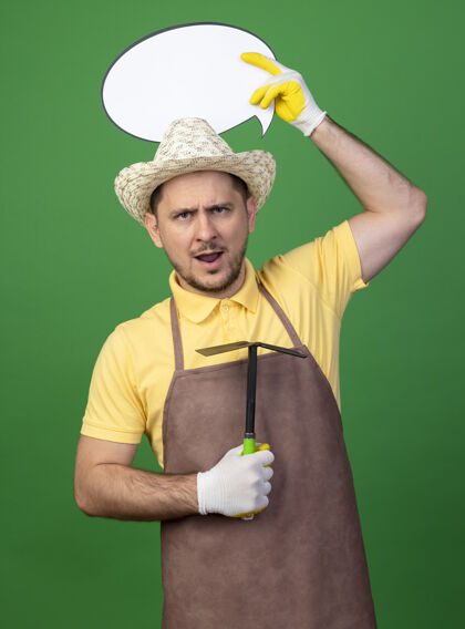 空白一个年轻的园丁 穿着连体衣 戴着帽子 戴着工作手套 手里拿着床垫 头上挂着一张表情严肃愤怒的白话泡泡牌连身衣绿色床垫