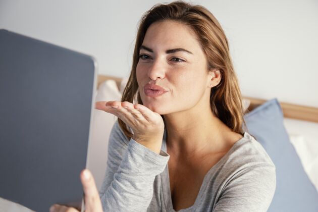 房子女子向平板电脑视频通话鞠躬亲吻女人吹吻平板电脑