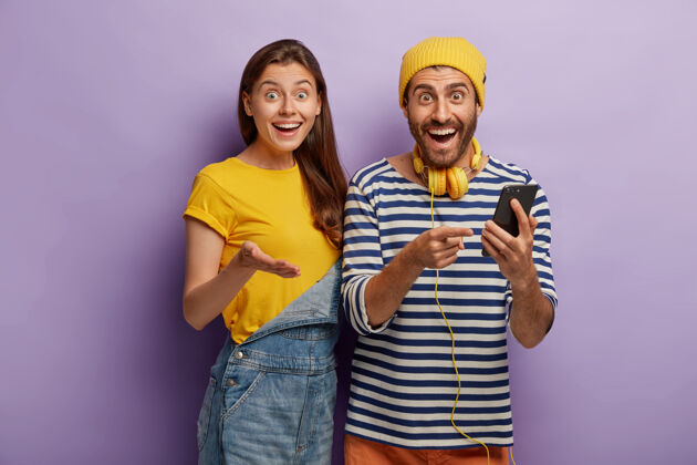 人快乐的欧洲女性和她的男朋友在网上聊天时用现代小玩意发短信 表情惊喜 戴立体声耳机紫色微笑条纹