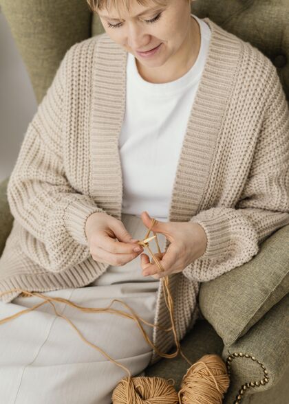 爱好特写微笑的女人在扶手椅编织质地工艺衣服