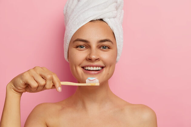 牙科快乐欧洲女人的剪短形象刷牙 拿着牙膏的牙刷 头上戴着裹着的毛巾 拥有健康清新的皮肤 赤身裸体地站着牙刷健康请