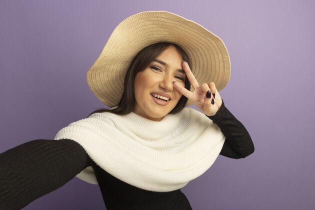 帽子戴着白领巾和夏帽的年轻女子面带微笑 脸上露出v字标志快乐站围巾