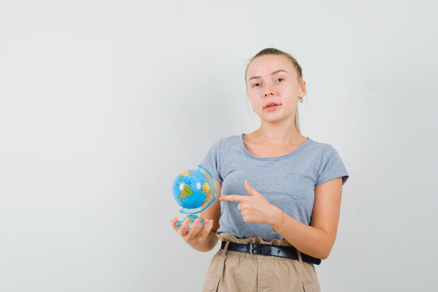 年轻年轻的女性穿着t恤 裤子指着地球仪 看上去很自信正视图人时尚人