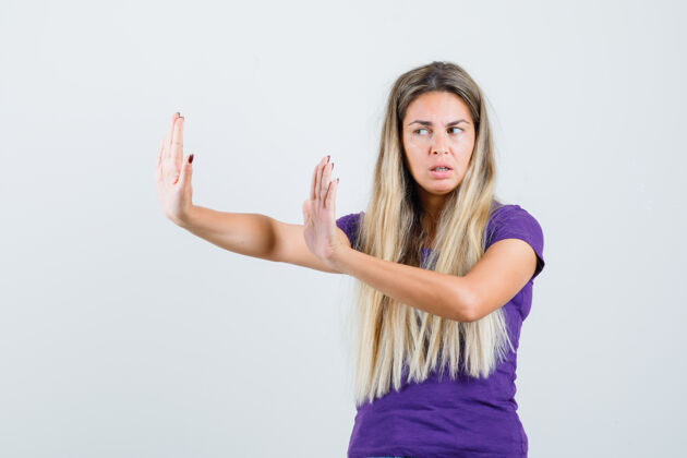 外观年轻的女士伸出手来保护自己在紫罗兰色t恤衫和看起来恼怒 前视图美丽女人一起