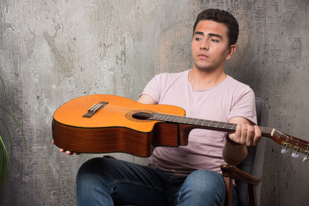 男年轻的音乐家看着大理石背景上的吉他乐器男人