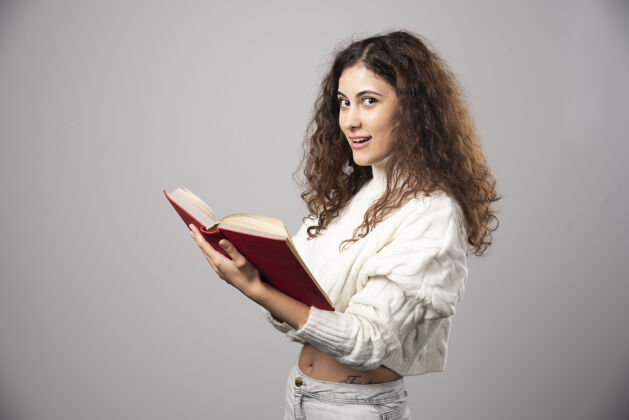 年轻年轻的微笑的女人拿着一本红色的书在灰色的墙上高质量的照片微笑女孩女性