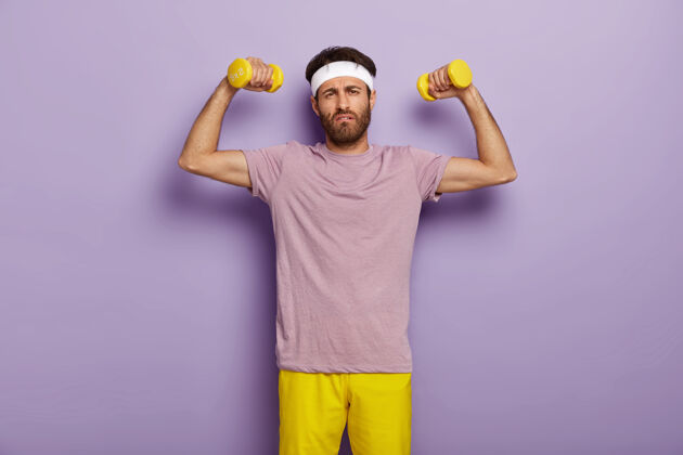服装情绪化的不刮胡子的男人积极参加体育运动 过着健康的生活方式 想要有强壮的肌肉 抱着黄色的鸭舌帽 表情疲惫的样子 穿着休闲服站立肌肉训练